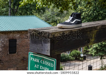 One tennis shoe sitting on a fence at a park