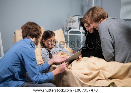 A happy little girl learning to use a tablet while she is staying in a hospital, her brother is helping her figure things out.