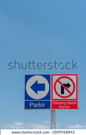 Blue color Parking (Indonesian : Parkir) Sign on left and Red color No Turn Right (Indonesian : Dilarang belok kanan) Sign, isolated with blue sky background. vertical version of the photo