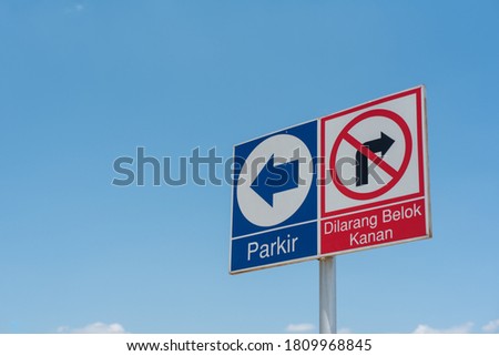 Blue color Parking (Indonesian : Parkir) Sign on left and Red color No Turn Right (Indonesian : Dilarang belok kanan) Sign, isolated with blue sky background. Horizontal version of the photo