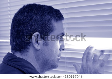 Man (male age 35-40) looking out through window with Venetian blinds. Concept photo Big Brother regime state, hiding, conspiracy, curious, spy, secret service agent, nosy man.Real people.Copy space 