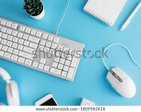 top view of office desk table with notebook, plastic plant, smartphone and keyboard on blue table background, graphic designer, Creative Designer concept.