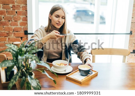 Young woman in casual outfit takes photos of food on smartphone in cafe 