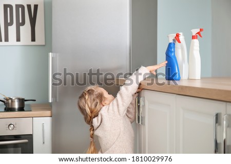 Little girl trying to reach out for bottles of detergent at home Royalty-Free Stock Photo #1810029976