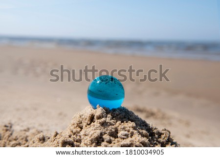 Blue glass ball on sand near the sea. Abstract conceptual photo.