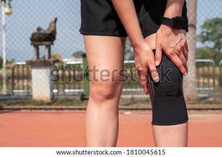 Runner woman holding her knee while she having suffering from knee pain and she wearing knee braces for supports to be worn when you have pain in your knee. Royalty-Free Stock Photo #1810045615