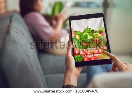 Woman using tablet and touching application screen for ordering salad online on sofa at the home.