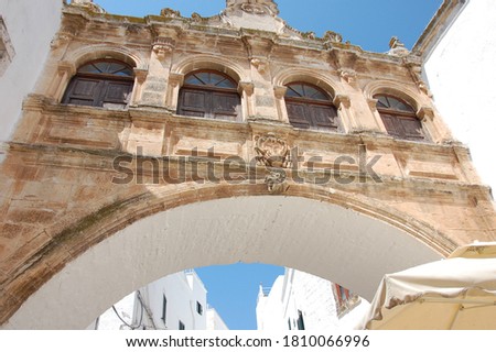 Alley in Ostuni called the white village in Puglia in Southern Italy. Photo taken from bottom up showing the upper part of building facade and a pale brown bridge with a blue clear sky in background