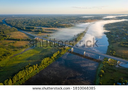 Early morning landscape. Foggy river. Highway bridge across the Volkhov river. River valley in the morning fog at sunrise. View from above. Rays of the sun breaking through the fog in over the trees Royalty-Free Stock Photo #1810068385