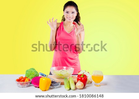 Happy young woman holding strawberry while showing OK sign with hand before prepare to make salad in the studio with yellow background