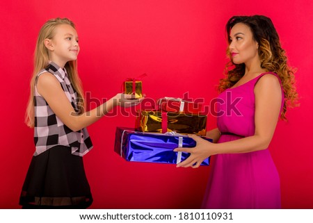 Cheerful mom and her cute daughter girl holding present gift. Red background