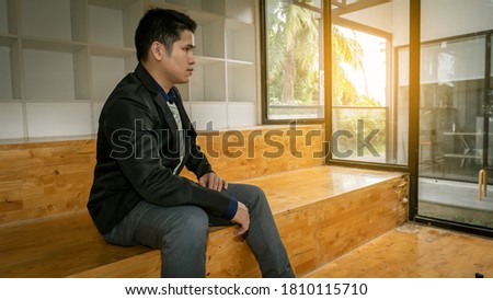 A picture of a positive young business man sitting in a modern corporate environment with sunlight shining through the windows of his office.