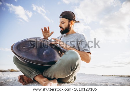stylish bearded man holding a unique handmade musical instrument playing on top of a mountain