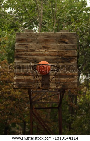 An orange basketball ball flies into an old basketball hoop made of wood and metal, with metal chains instead of a rope net in the yard