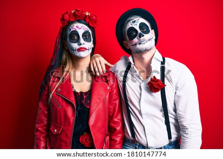 Couple wearing day of the dead costume over red looking sleepy and tired, exhausted for fatigue and hangover, lazy eyes in the morning. 