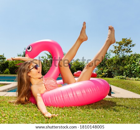 Girl in a funny falling pose wear sun glasses lay on the pink flamingo near swimming pool