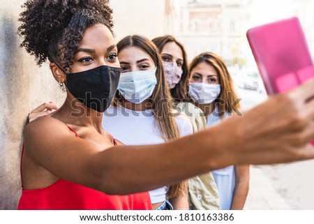 Four young multiracial friends women with face mask for protection by infection from Coronavirus, Covid-19 - Millennials taking a selfie with smartphone