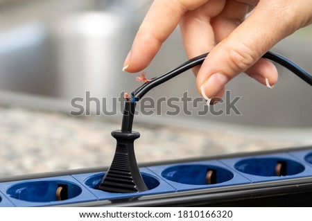 Close up of a woman hand holding a dangerous damaged electrical cord at kitchen Royalty-Free Stock Photo #1810166320
