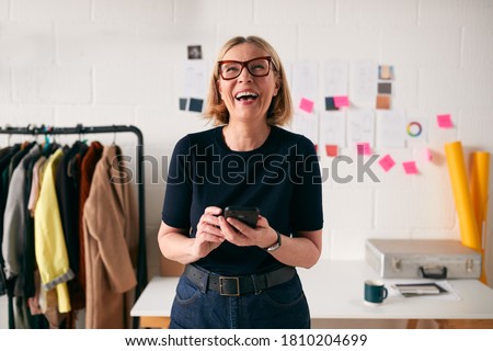 Laughing Mature Businesswoman With Mobile Phone In Front Of Desk In Start Up Fashion Business Royalty-Free Stock Photo #1810204699