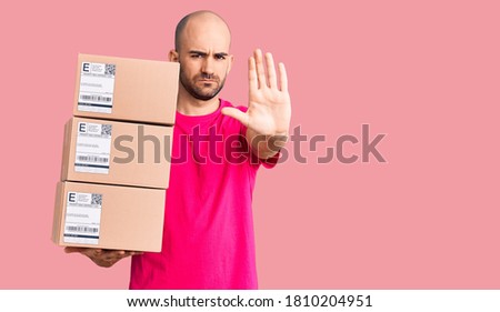 Young handsome man holding delivery package with open hand doing stop sign with serious and confident expression, defense gesture 