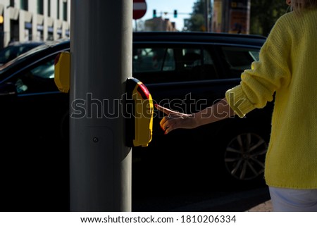 Young woman in a yellow sweater presses the button at the pedestrian crossing. A woman is standing at the crosswalk waiting for the green light. A young woman pressing the button to cross the road