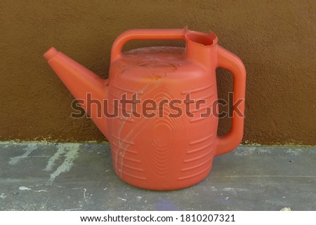 Red watering can stranded outside the house.