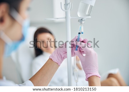 Experienced Caucasian heath care worker preparing a dark-haired female patient for the intravenous vitamin therapy Royalty-Free Stock Photo #1810213150