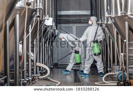 Craft brewery, eco product and disinfection. Workers in hazmat suits clean plant and kettles during quarantine, side view, free space Royalty-Free Stock Photo #1810288126