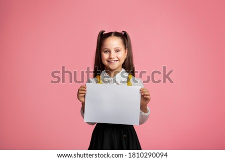 Primary education. Small schoolgirl with happy smile holding sign with free space, isolated on pink background, studio shoot