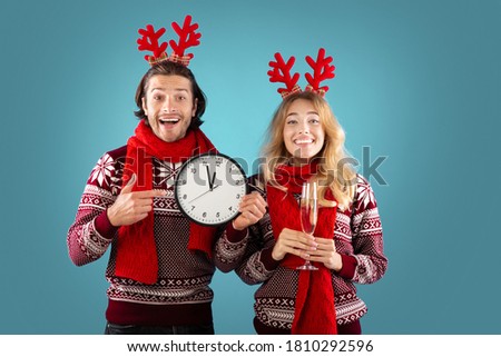 New Year celebration. Affectionate young couple with champagne and clock showing five minutes till midnight, blue background