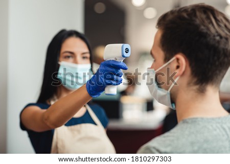New rules of life. Hairdresser checking body temperature of client at barber shop