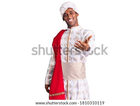 African handsome man wearing tradition sherwani saree clothes smiling cheerful offering palm hand giving assistance and acceptance. 