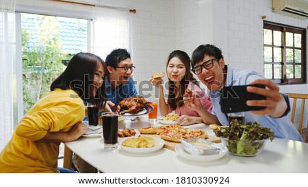 Happy young group having lunch at home. Asia family party eating pizza food and making selfie with her friends at birthday party at dining table together at house. Celebration holiday and togetherness