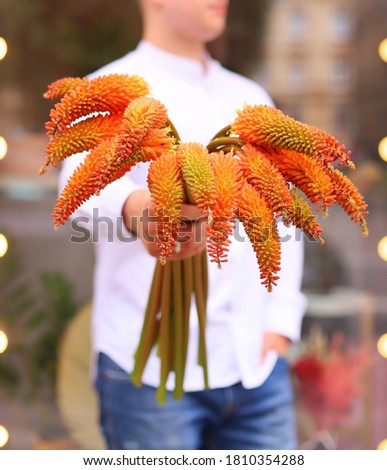 Young man florist holding exotic bouquet in orange color.
