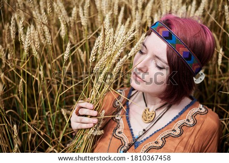 Young woman with red burgundy hair, wearing boho hippie clothes, lying, resting on wheat stalks in the middle of field. Close-up picture of female face on natural background. Creative portrait.
