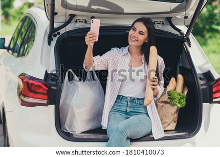Portrait of her she nice attractive cheerful cheery lady blogger sitting in trunk carrying fresh bread ingredients bio farm products baguette supply taking making selfie outdoor outside