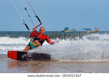 Kitesurfing on the waves of the sea in Mui Ne beach, Phan Thiet, Binh Thuan, Vietnam. Kitesurfing, Kiteboarding action photos. Kitesurf In Action against vietnamese boats