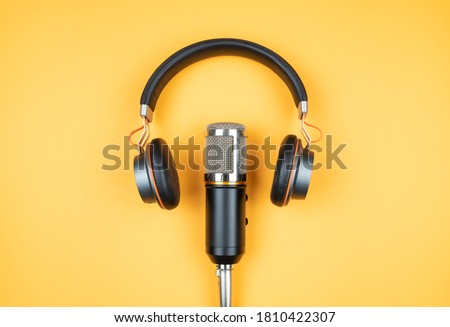 podcasting concept, directly above view of headphones and recording microphone on orange background Royalty-Free Stock Photo #1810422307