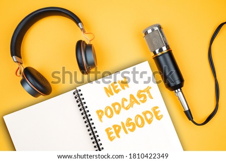 NEW PODCAST EPISODE text on notepad next to headphones and recording microphone, podcasting concept on orange background