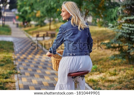 Back view portrait of beautiful blonde Caucasian female riding on the bike in the green city park