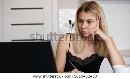 Portrait of an attractive woman at the table with cup and laptop. Confused young woman having problem with computer, looking at laptop screen