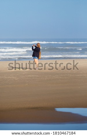 Woman taking photo of the pacific ocean in Oregon with her smartphone, vertical