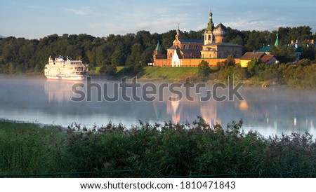 A tourist motor ship against the background of the male Nikolsky monastery in Staraya Ladoga in the Leningrad Region on a foggy morning on the Volkhov River. Traveling on the rivers of Russia Royalty-Free Stock Photo #1810471843
