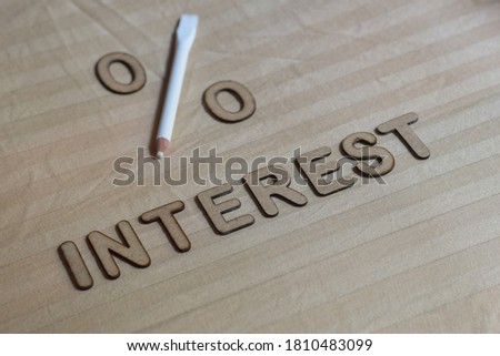 The word says INTEREST written in 3d wooden alphabet letters with a persentage sign laid on beige fabric background. Conceptual image of financial investment, selective focus.