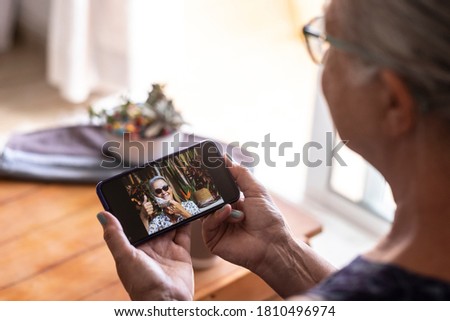 Defocused senior woman using smart phone to video call with sister absent due to coronavirus - on the screen smiling lady takes off the mask doing ok sign with hand
