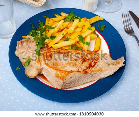 Delicious fried pork tenderloin with potatoes, served with greens on plate