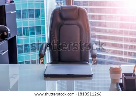 View of empty workplace in office. The chair sits next to the glass table on which the laptop is. Blurred office buildings are visible in the background. Royalty-Free Stock Photo #1810511266