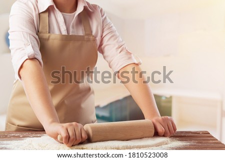 Happy attractive young woman wearing apron cooking dough on the kitchen