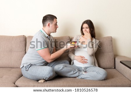 Husband offers a cake to his pregnant wife but she refuses and makes stop gesture because she feels sick. Feeling bad during pregnancy concept.