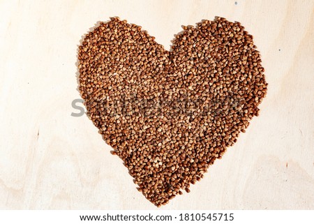 Buckwheat heart on wooden background with place for an inscription. Heart symbol made from buckwheat. Heart made of cereals. Healthy eating